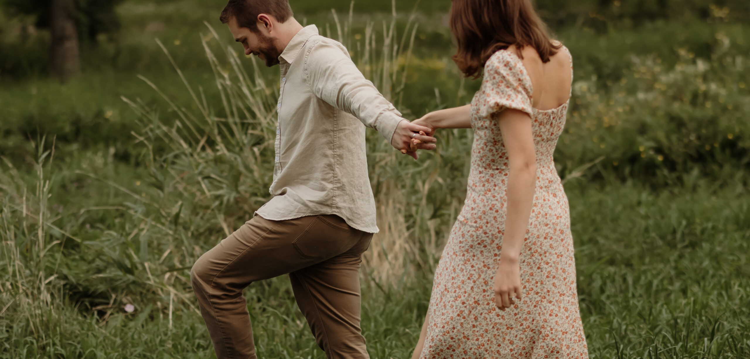 Engaged couple during a Maine engagement photoshoot, embracing in a field of tall grass with soft natural light, capturing an intimate and romantic moment