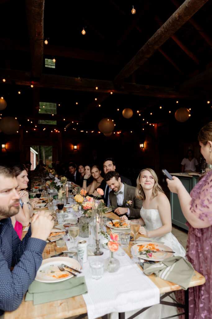 A candid photo of the bride, groom, and wedding guests listening to the maid-of-honor's speech.