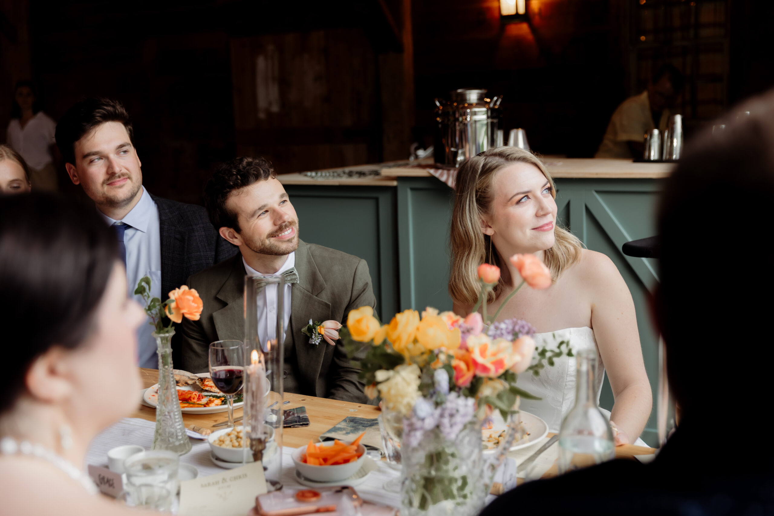 A candid photo of the bride, groom listening to the maid-of-honor's speech.