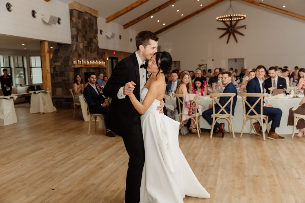 Bride and groom sharing their first dance in a bright, spacious room at the Essex Resort and Spa, a popular Vermont wedding venue, surrounded by warmly lit decor and smiling guests.