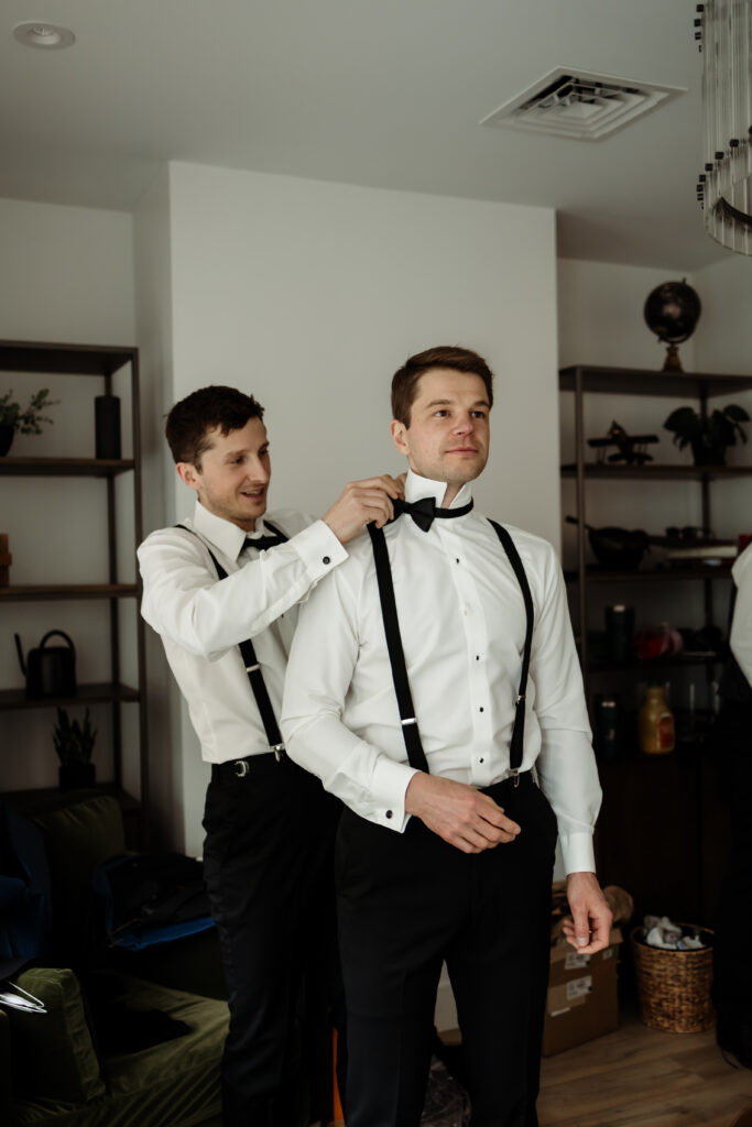 Groom adjusting groomsman’s tie while preparing for Beautiful Rainy Wedding Day in Vermont at the Essex Resort and Spa, a premier Vermont wedding venue.