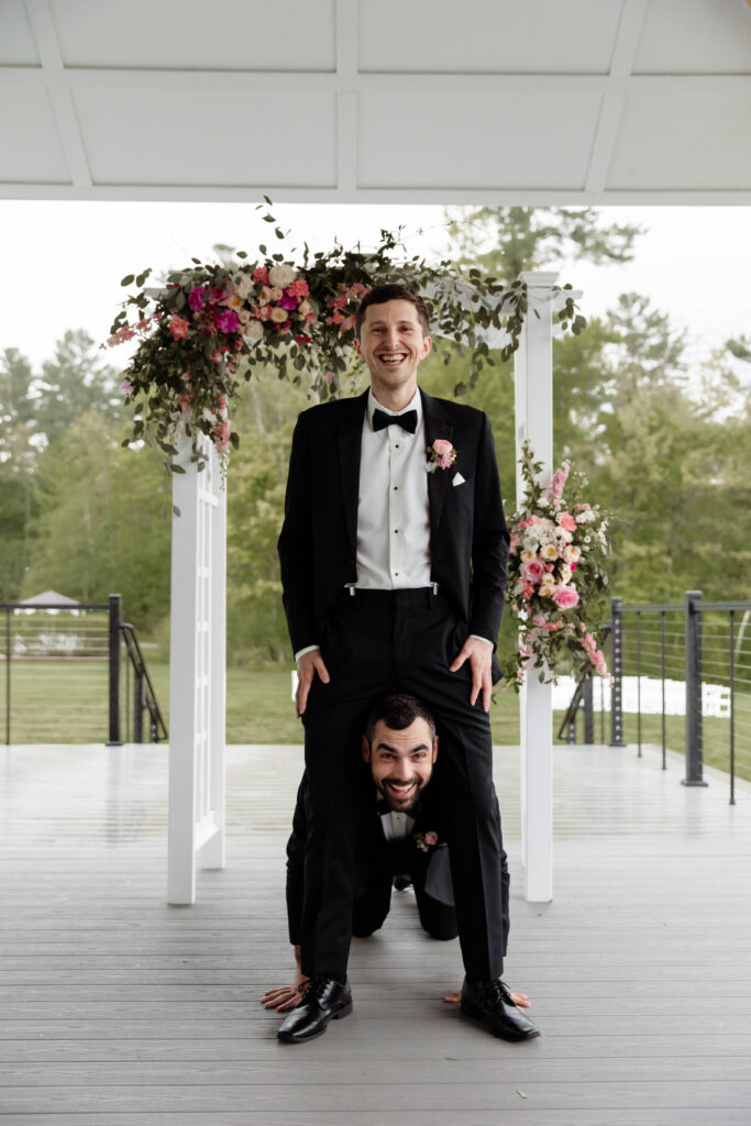 Groom and groomsman sharing a playful, silly pose while getting ready together at the Essex Resort and Spa, Beautiful Rainy Wedding Day in Vermont.
