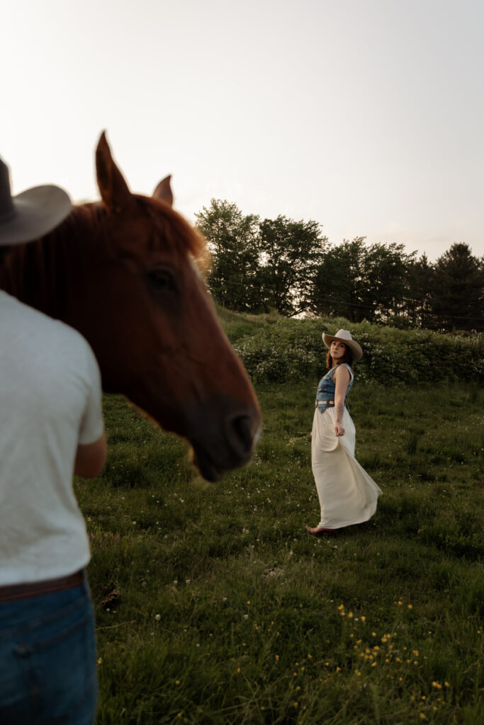 Vermont engagement photo of woman in focus with fiancé and horse in soft background on a scenic farm with outfit Tips for Vermont Engagement and Couples Photos
