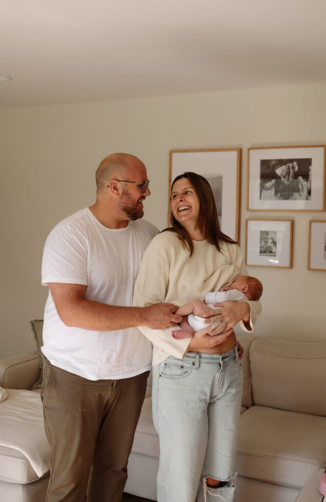 New parents hold their newborn together during in-home family photos, captured by a Maine family photographer.