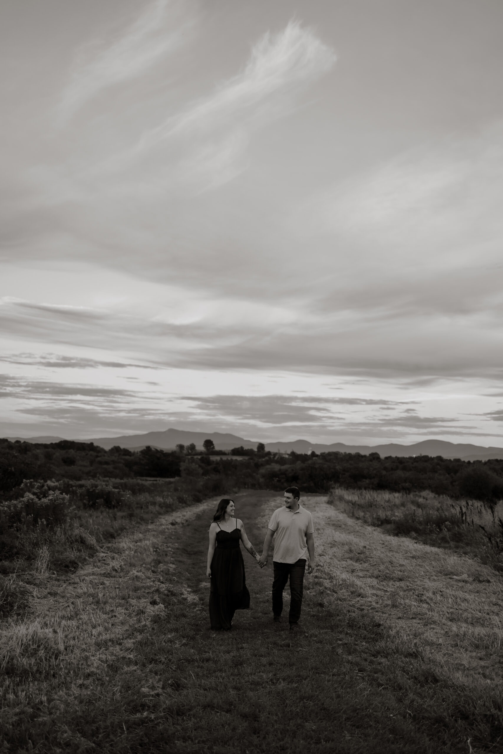 Black and White photo of couple embracing in a field during golden hour.