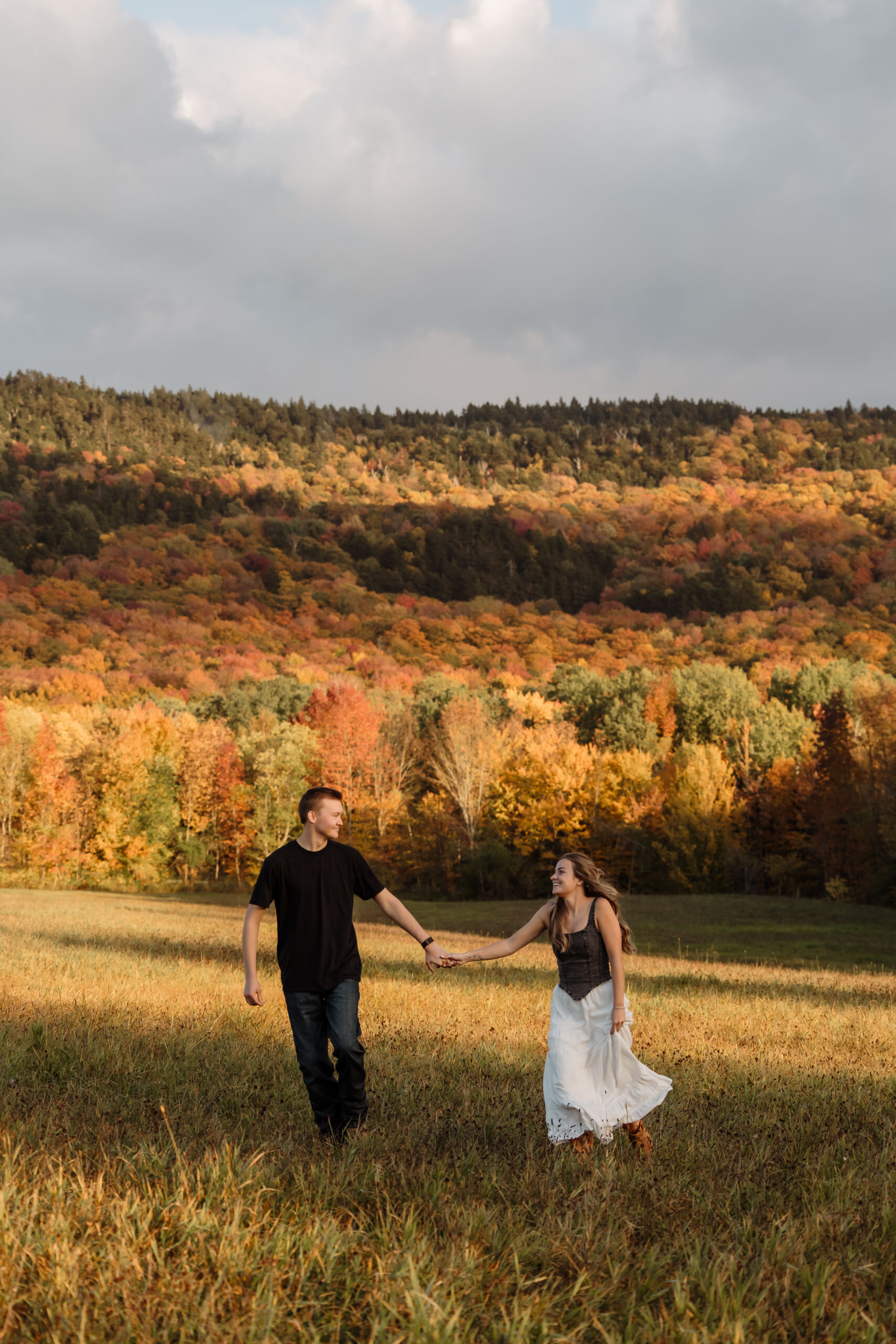 Couple holding hands in tall grass with golden fall foliage | Engagement photos in Rangeley Maine