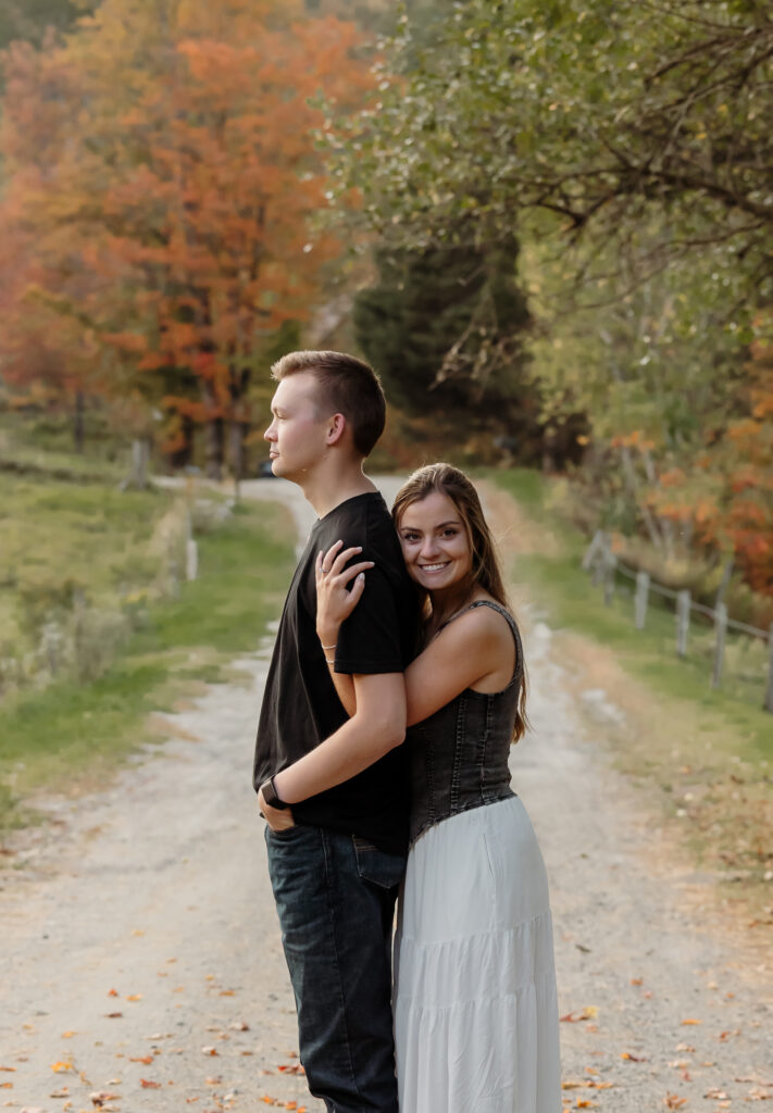 Couple laughing in a meadow with autumn trees in the background | Rangeley Maine engagement session