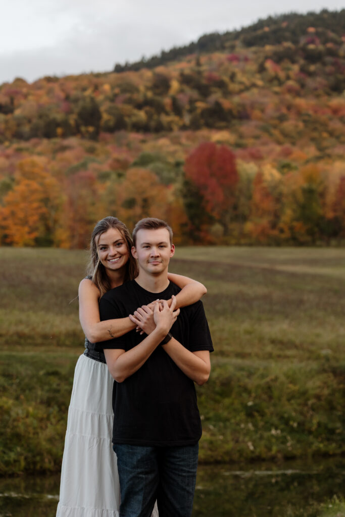 Engaged couple embracing in a forest of colorful autumn leaves | Rangeley Maine engagement photography