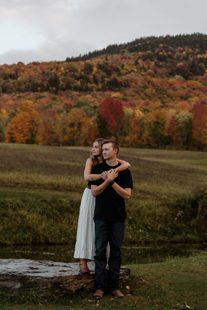 Couple walking along a lakeside trail surrounded by fall colors | Rangeley Maine engagement session