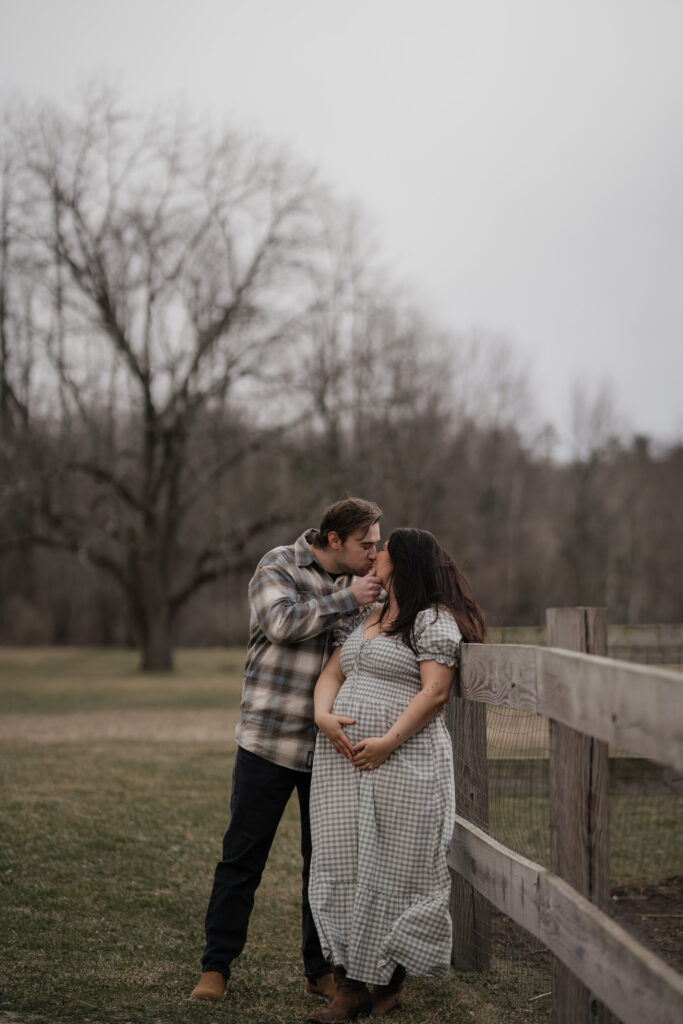 Maine maternity photographer captures pregnant woman at 36 weeks standing in a sun-drenched field, hands gently cradling her baby bump in a long flowing dress