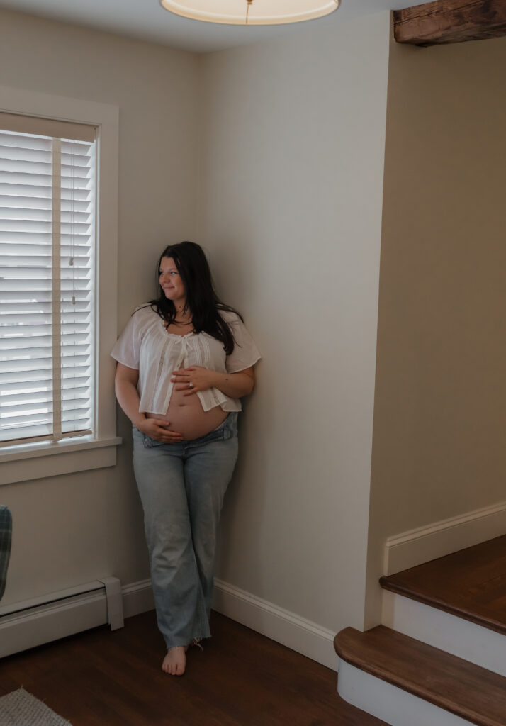 Pregnant woman gently holding her belly during indoor Maine maternity session