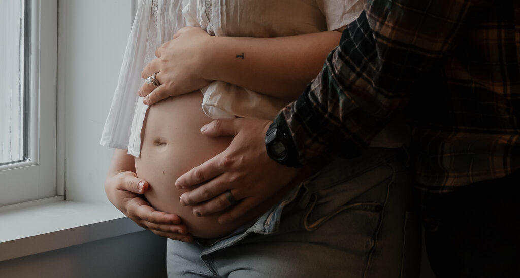 Close-up of pregnant belly with both parents' hands during intimate Maine maternity session.